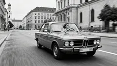 Klassischer BMW fährt durch eine historische Stadtstraße in Schwarz-Weiß, 1970er Jahre.
