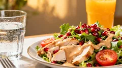 Frischer Salat mit Hähnchen, Granatapfel, Tomaten und Dressing, dazu Wasser und Orangensaft