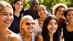 Gruppe von Menschen unterschiedlicher Herkunft lächelt zusammen im Freien bei Sonnenschein.